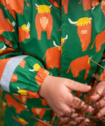 Small child wearing Frugi's waterproof puddle buster coat in highland grazing showing close up of the repeating Highland cow design 