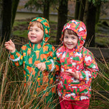 Child wearing Frugi's green highland grazing puddle buster waterproof coat next to child wearing the pink purrfect ponies coat