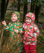 Child wearing Frugi's green highland grazing puddle buster waterproof coat next to child wearing the pink purrfect ponies coat