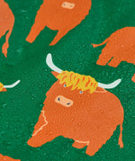 Frugi waterproof puddle buster coat in highland grazing showing the repeating highland cow design and water beading