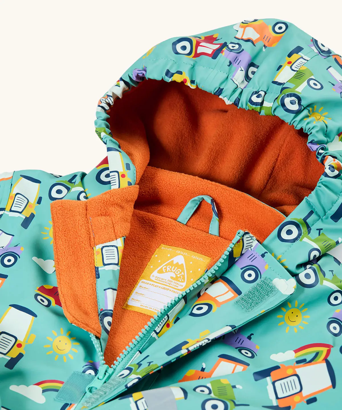 Frugi waterproof puddle buster coat in terrific tractors laid flat showing the front zip with velcro fastener and orange fleece liner with name tag