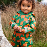 Small child wearing the Frugi waterproof green highland cow puddle buster all in one with the hood down