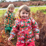 Child wearing Frugi's pink pink puddle buster coat with a repeating horse and tree design in a grassy field.