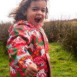 Small child wearing Frugi waterproof puddle buster coat in pink purrfect ponies design showing the hood is down 