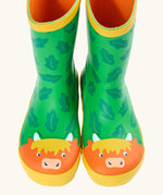 Front of Frugi puddle buster wellington boots showing the repeating leaf design and highland cow toe cap on green natural rubber material