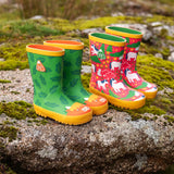Pair of Frugi natural rubber, waterproof puddle buster wellingtons outdoors showing a green with a repeating leaf design and highland cow toe cap and a pink with repeating white ponies design