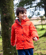 Child wearing the Frugi kids 3 in 1 rambler coat in fire orange in the outdoors with the front zip and popper fully fastened. Coat has a relaxed fit