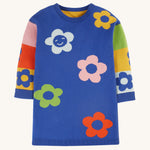 The blue body and colour-block side of the Frugi Zola Reversible Knitted Dress - Blue Tang/Retro Floral. A soft, royal blue, organic cotton knit dress, with colour-block sleeves in yellow, red, green, pink and light blue colour, and colourful bold flower prints 