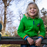 A child standing over a gate and wearing the green Jersey style Frugi helston reversible hoodie available at Babipur.
