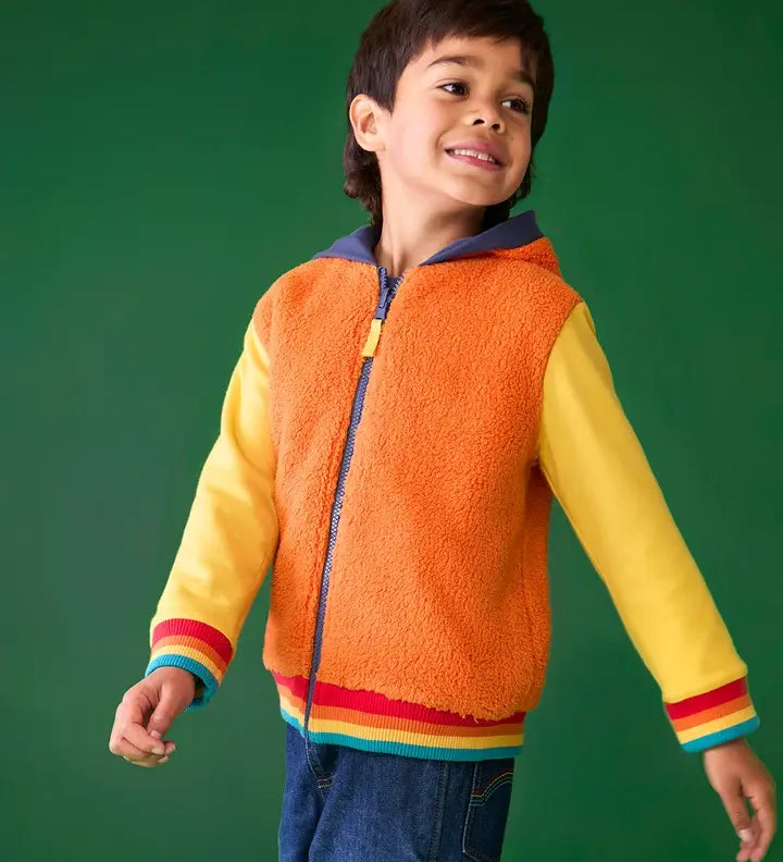 Frugi reversible hoodie in soft orange fleece, cotton yellow sleeves with rainbow elastic cuffs, worn by boy in jeans.