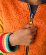 Frugi reversible organic cotton hoodie in orange recycled fluffy fleece with rainbow elasticated cuffs, worn by child.