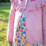 A child wearing the Frugi pink marl Romi cardigan with a matching skater dress available at Babipur. A GOTS organic cotton pink cardigan with a red toadstool embroidery running along the top of the cardigan.
