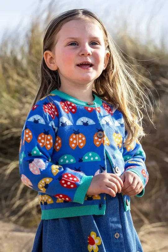 Child wearing Frugi Ladybird knitted cardigan in blue on the beach to represent Frugi sale at Babipur.