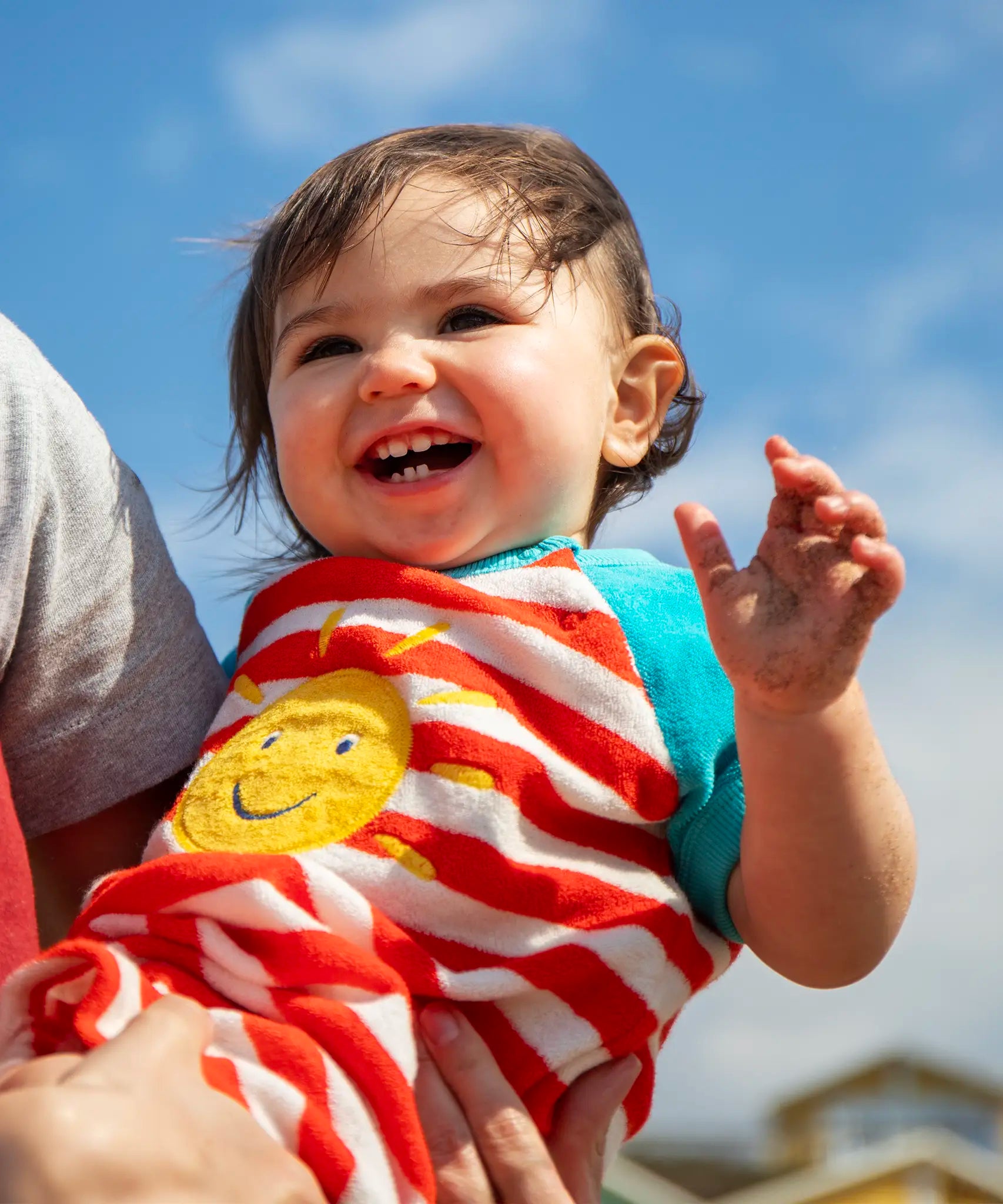 Baby wearing Frugi's towelling romper with blue sleeves, white and red stripe body and yellow sun patch 