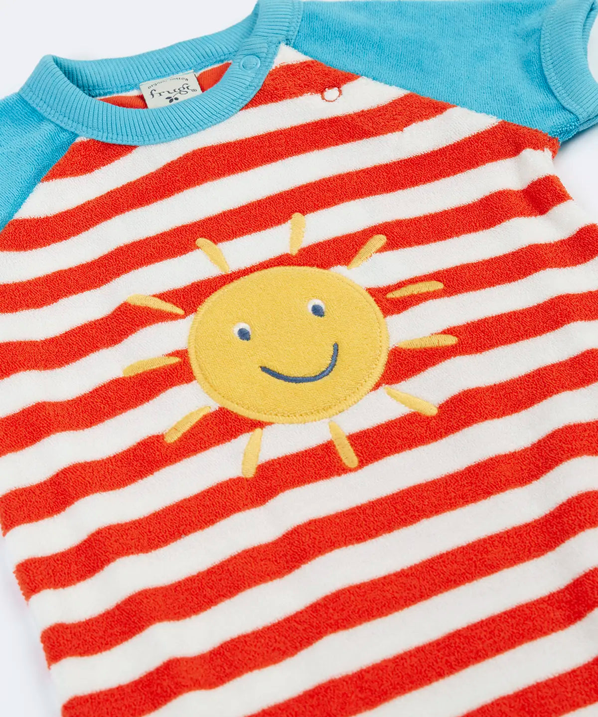 Frugi baby towelling romper laid flat showing blue sleeves, white and red stripe body, yellow sun on the front and popper fasteners