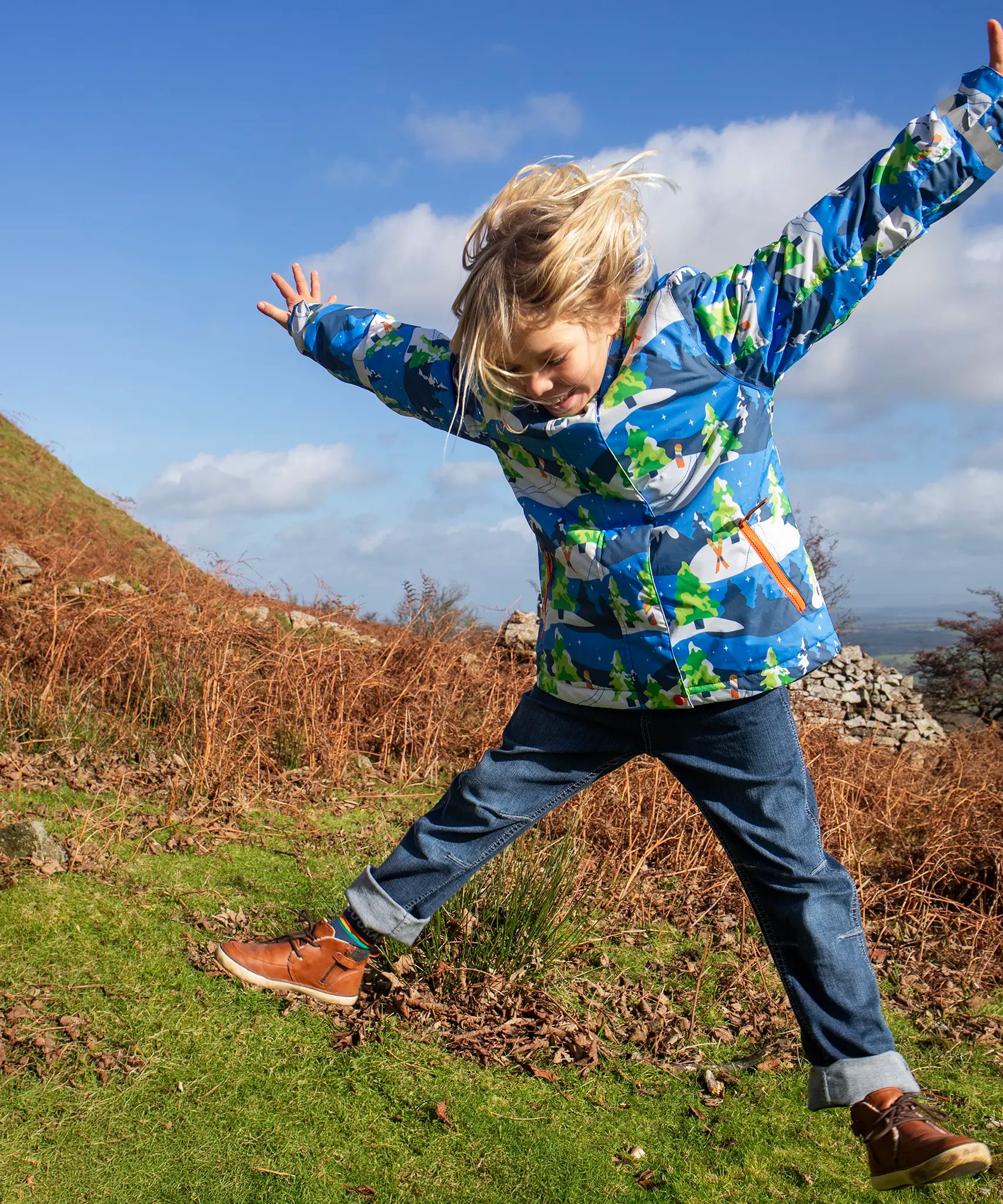 Child jumping in a field and wearing the Frugi recycled polyester snow and ski coat in starry slopes 
