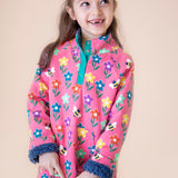 A child wearing the Frugi fun flowers snuggle fleece available at Babipur. A  thick pink jacket made from GOTS organic cotton with a playful flowery design and a purple fleece inner. Features a popper fastener in green trim