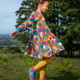 Frugi sofia skater dress in rainbow fun frenzy print, knee length with long sleeves, worn by child playing outside.
