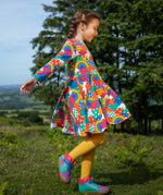 Frugi sofia skater dress in rainbow fun frenzy print, knee length with long sleeves, worn by child playing outside.