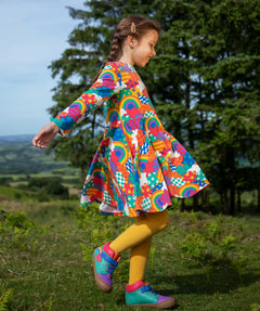 Frugi sofia skater dress in rainbow fun frenzy print, knee length with long sleeves, worn by child playing outside.