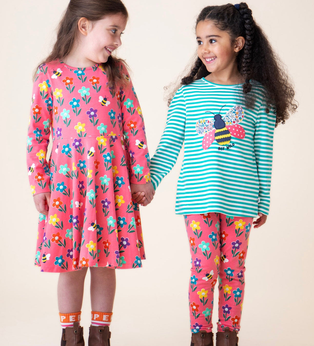 A child wearing the Frugi sofia skater dress in tulip/fun flowers and standing next to another child wearing the tulip fun flowers leggings with the Frugi dragon stripe/bee top available at Babipur
