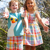Child wearing Frugi's light blue t-shirt with white goose patch on front and child wearing a pastel check dress