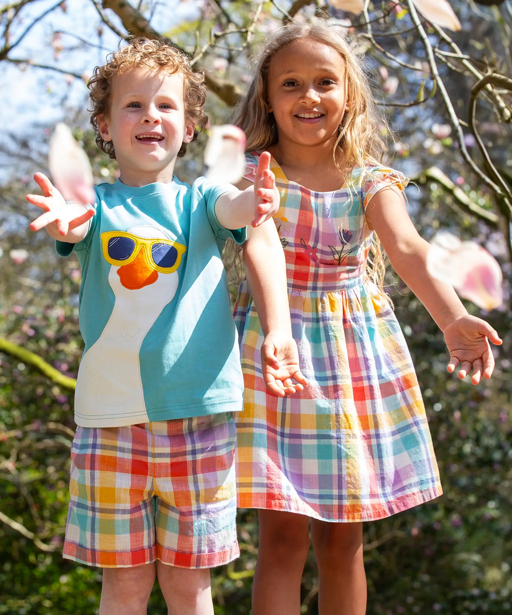 Child wearing Frugi's light blue t-shirt with white goose patch on front and child wearing a pastel check dress