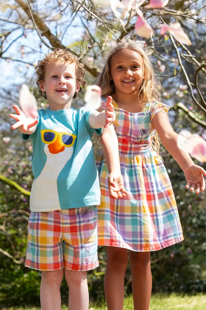 Kids wearing Spring Frugi clothes from Babipur, a goose t-shirt with check shorts, and a matching check dress.