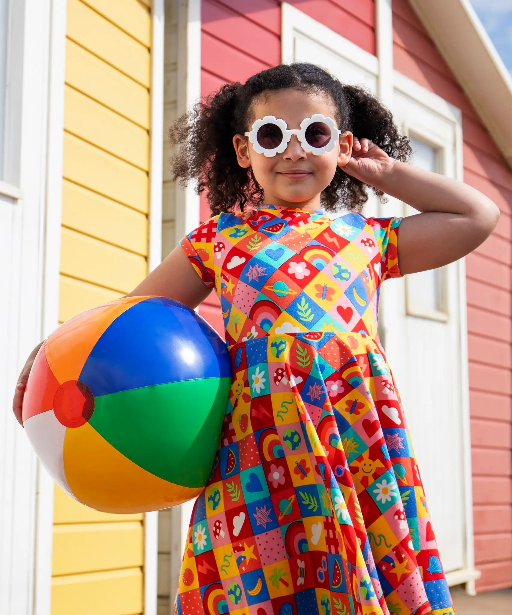 Child wearing Frugi's favourite things Spring skater dress and holding a rainbow beach ball