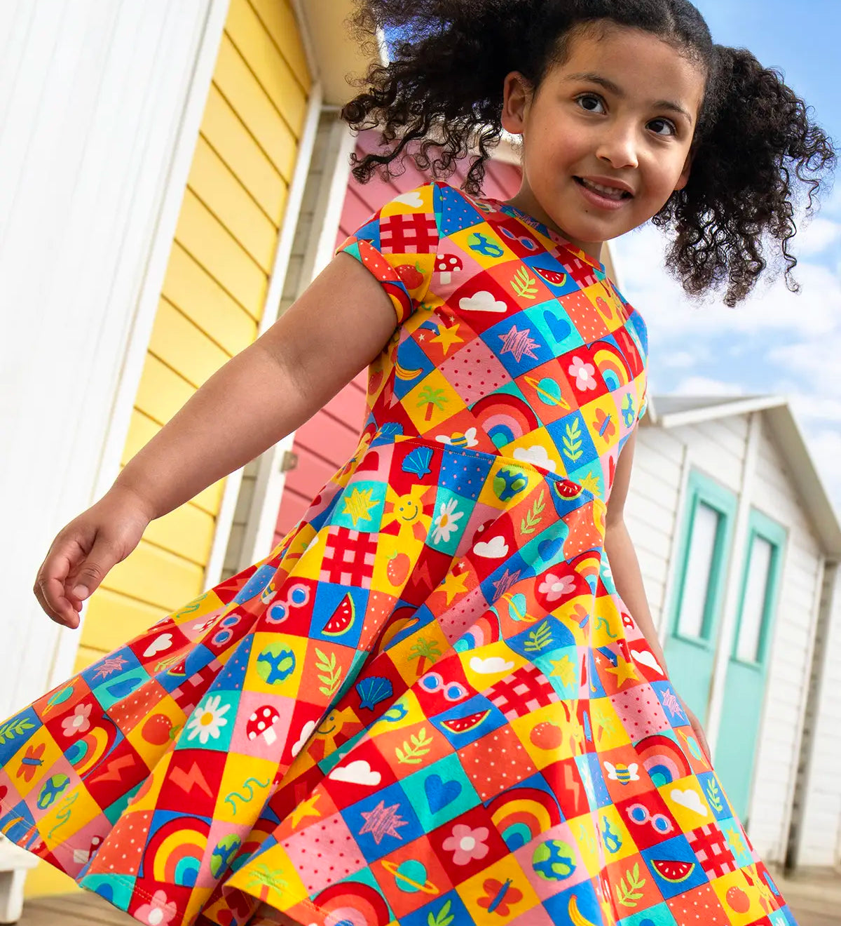 Child wearing Frugi's favourite things Spring skater dress with beach huts in the background