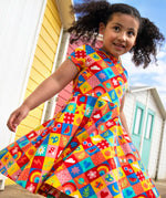 Child wearing Frugi's favourite things Spring skater dress with beach huts in the background