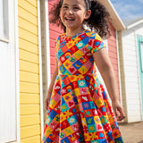 Child wearing Frugi's favourite things Spring skater dress standing in front of  beach huts 