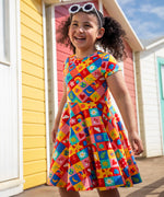 Child wearing Frugi's favourite things Spring skater dress standing in front of  beach huts 