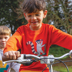 A child riding a bike whilst wearing the Frugi Owen Top - Bonfire/Lemur