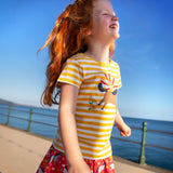 Child wearing Frugi's yellow and white stripe short sleeve t-shirt with a horse patch on the front and standing on the promenade