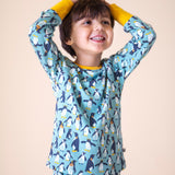 A child wearing the Frugi sundown pyjamas in penguin waddle available at Babipur. A GOTS organic cotton pyjama top and bottom set in light blue with a penguin design all over and yellow trim