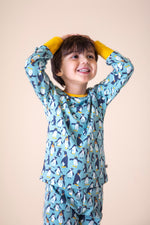 A child wearing the Frugi sundown pyjamas in penguin waddle available at Babipur. A GOTS organic cotton pyjama top and bottom set in light blue with a penguin design all over and yellow trim