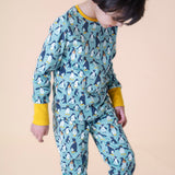 A child wearing the Frugi sundown pyjamas in penguin waddle available at Babipur. A pyjama set in light blue with a penguin design all over and yellow trim