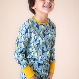 A child wearing the Frugi sundown pyjamas in penguin waddle available at Babipur. A GOTS organic cotton pyjama set in light blue with a penguin design all over and yellow trim
