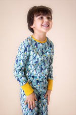 A child wearing the Frugi sundown pyjamas in penguin waddle available at Babipur. A GOTS organic cotton pyjama set in light blue with a penguin design all over and yellow trim