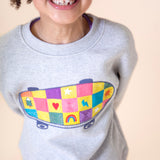 A close up of a child wearing the Frugi Superb Stitched Skateboard sweatshirt available at Babipur showing the embroidered skateboard design detail