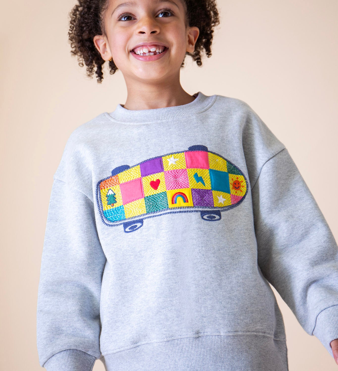 A child wearing the Frugi Superb Stitched Skateboard sweatshirt available at Babipur. A GOTS organic cotton sweater i with a embroidered skateboard with checkerboard design.