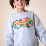 A child wearing the Frugi Superb Stitched Skateboard sweatshirt available at Babipur. A GOTS organic cotton sweater i with a embroidered skateboard with checkerboard design.
