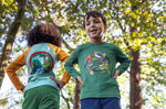 A child standing outside by trees and wearing the Frugi kids terrific applique top in holly green/birds available at Babipur.