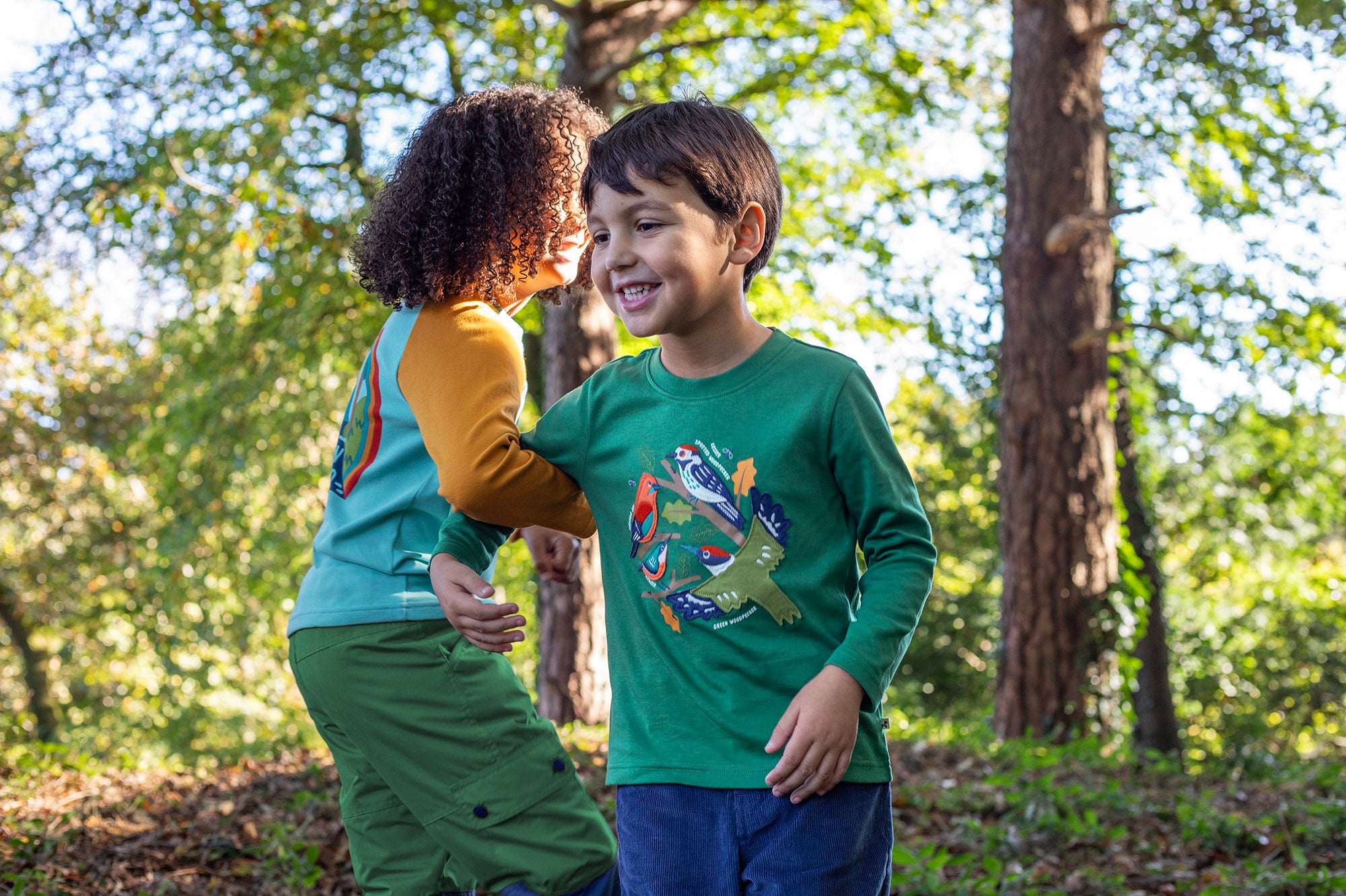 A child playing outside by trees and wearing the Frugi kids terrific applique top in holly green/birds available at Babipur. A dark green long sleeved GOTS organic top with different bird appliques