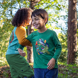 A child playing outside by trees and wearing the Frugi kids terrific applique top in holly green/birds available at Babipur. A dark green long sleeved GOTS organic top with different bird appliques