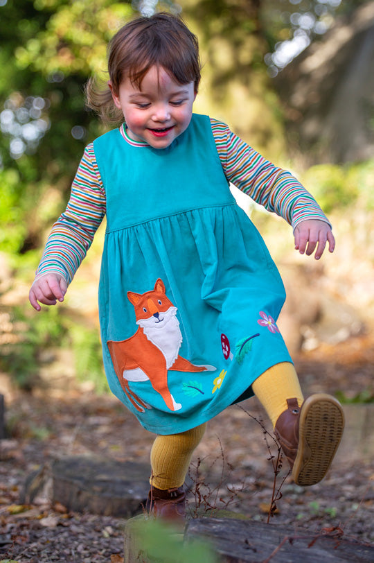 Child wearing Frugi Lily organic cotton cord Dress Boat Blue with fox applique, striped rainbow top and gold yellow tights, to represent Frugi baby and kids clothing at Babipur.