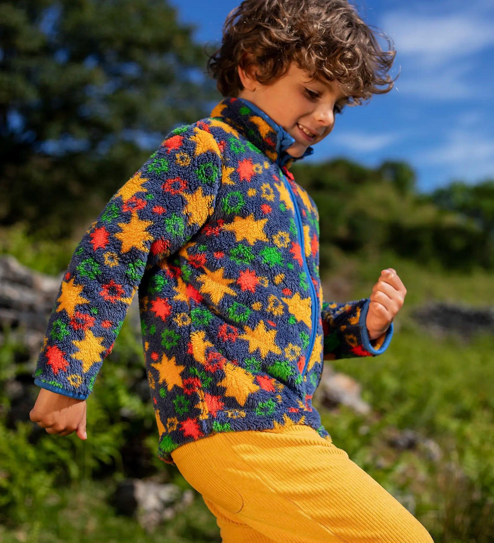 Frugi zipped ted fleece in navy with orange star print worn by child outside with yellow cord trousers.