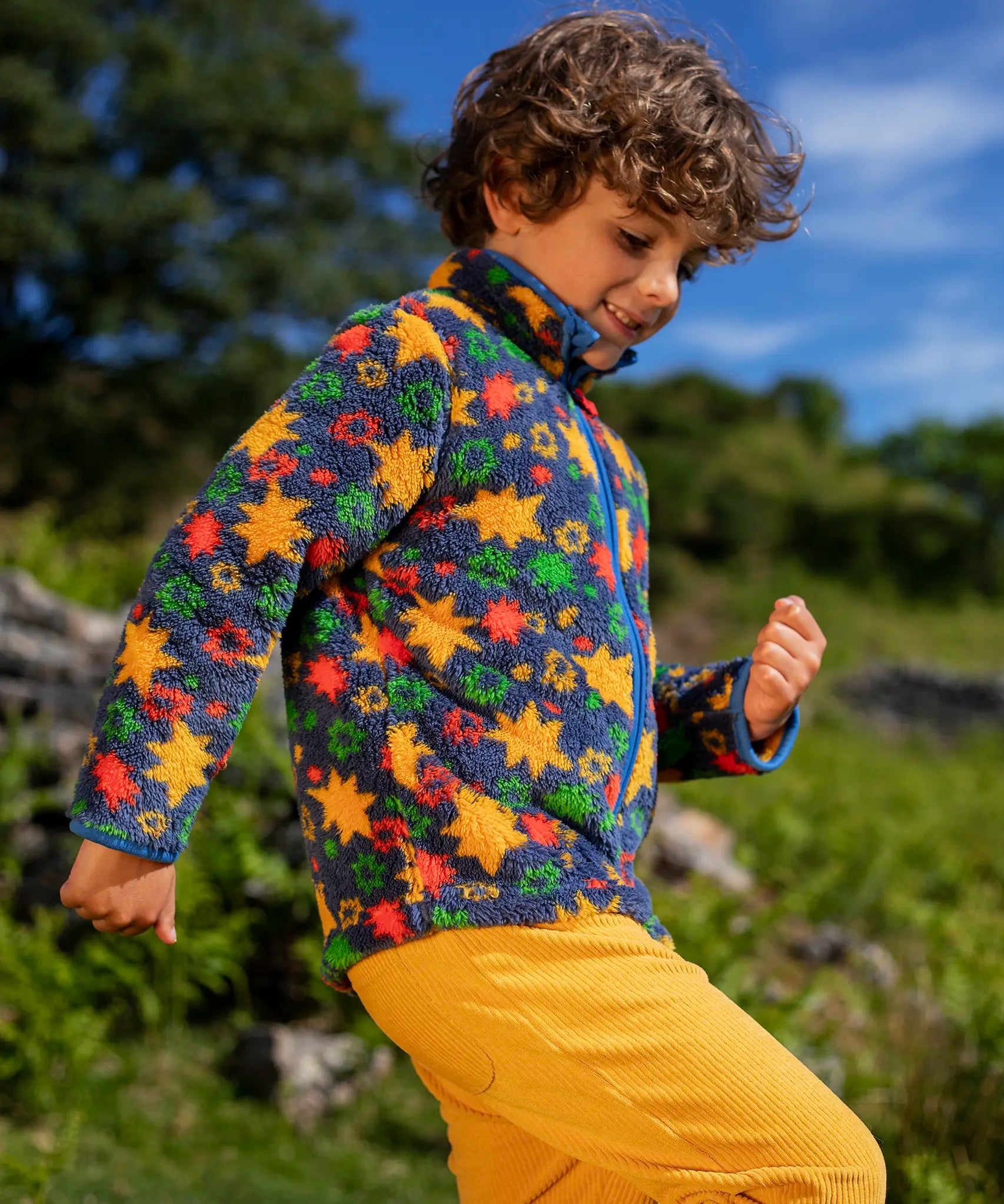 Frugi zipped ted fleece in navy with orange star print worn by child outside with yellow cord trousers.