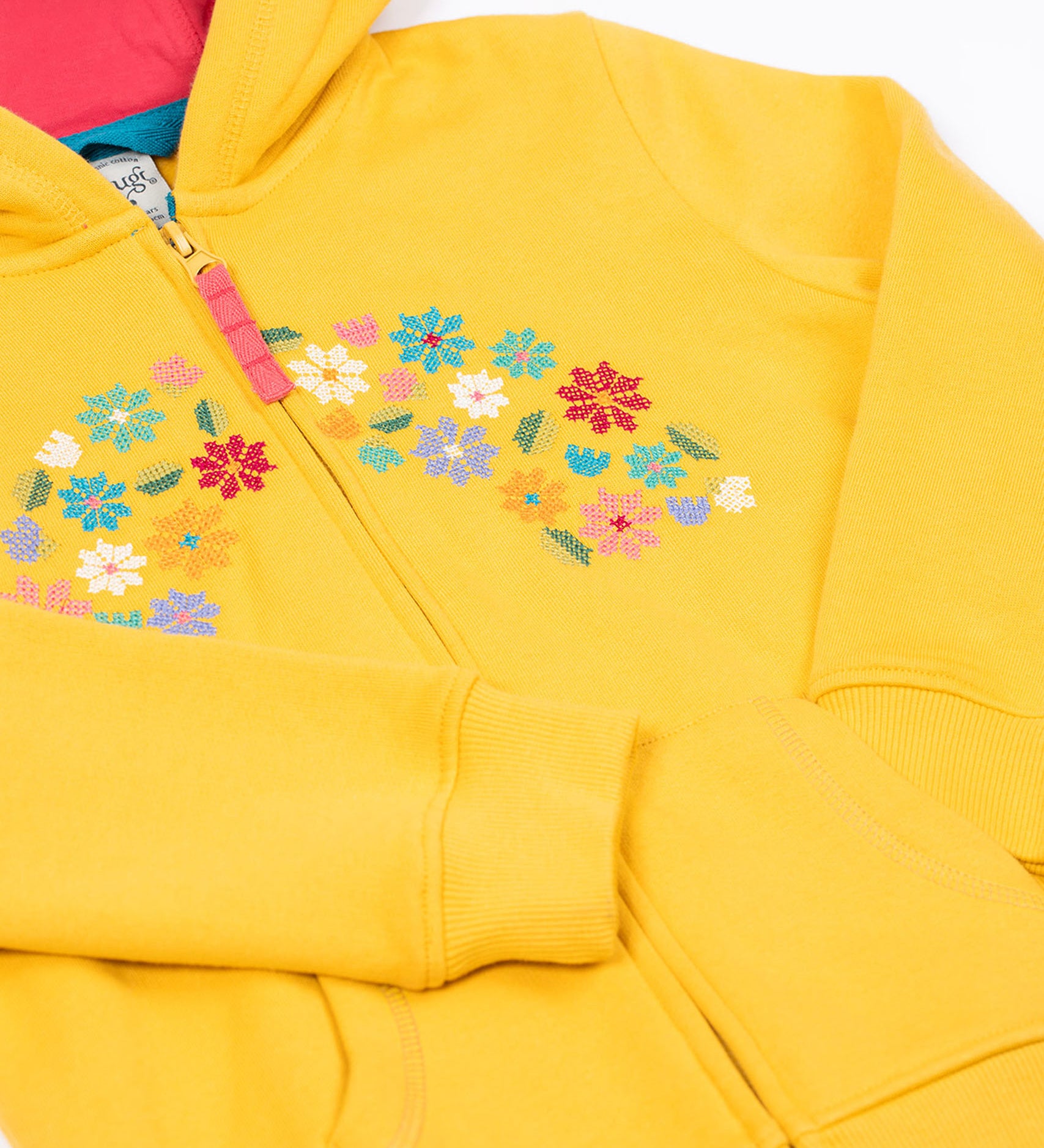 A close up of the Frugi kids carbis hoodie in bumblebee/flowers showing the delicate flower embroidery and pouch pocket detail on yellow organic cotton fabric.